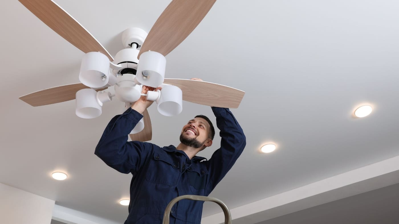 Technician installing a white ceiling fan in a bright modern room