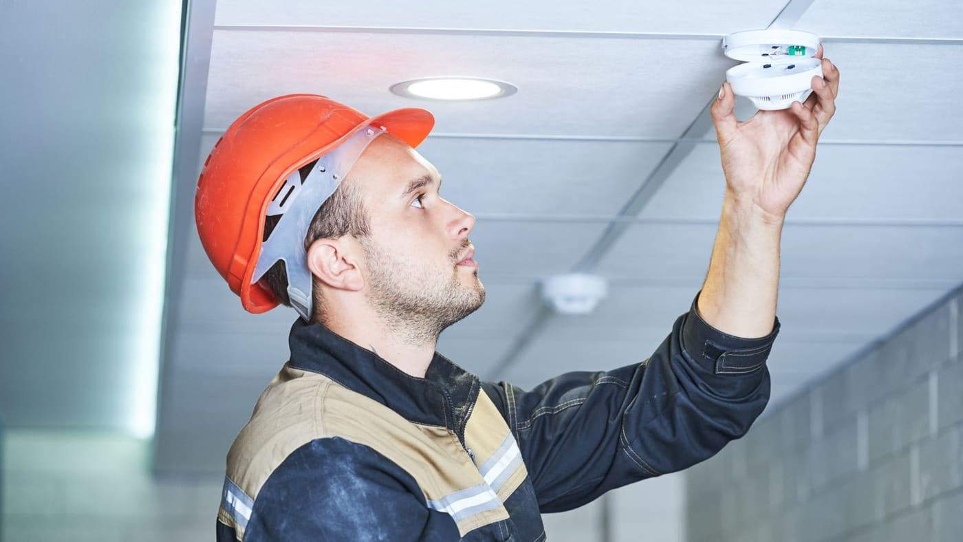 Electrician in hard hat installing a recessed light in a drywall ceiling