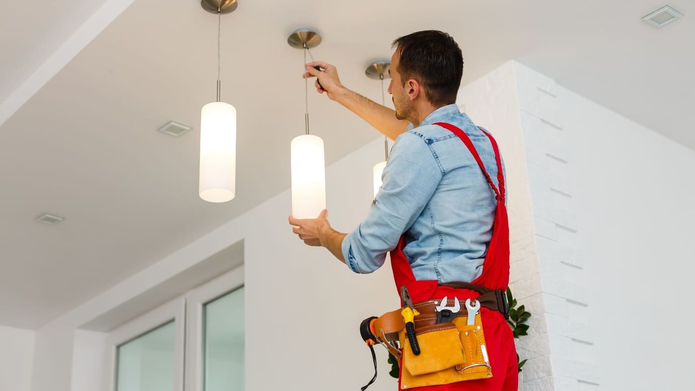 Electrician installing cylinder pendant light fixtures in a bright living space