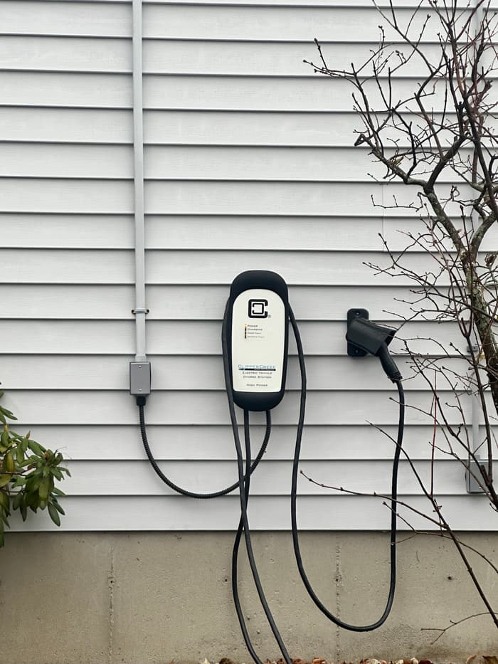 A Level 2 charging station set at reach height beside the driveway with the cord holster mounted alongside.