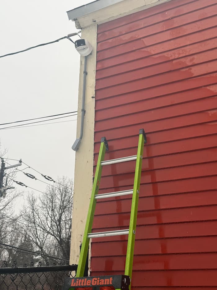Camera and light work at the roofline of a commercial building, ladder set for safe access.