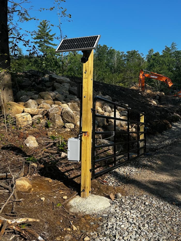 A solar-powered gate operator wired at the end of a new gravel driveway.