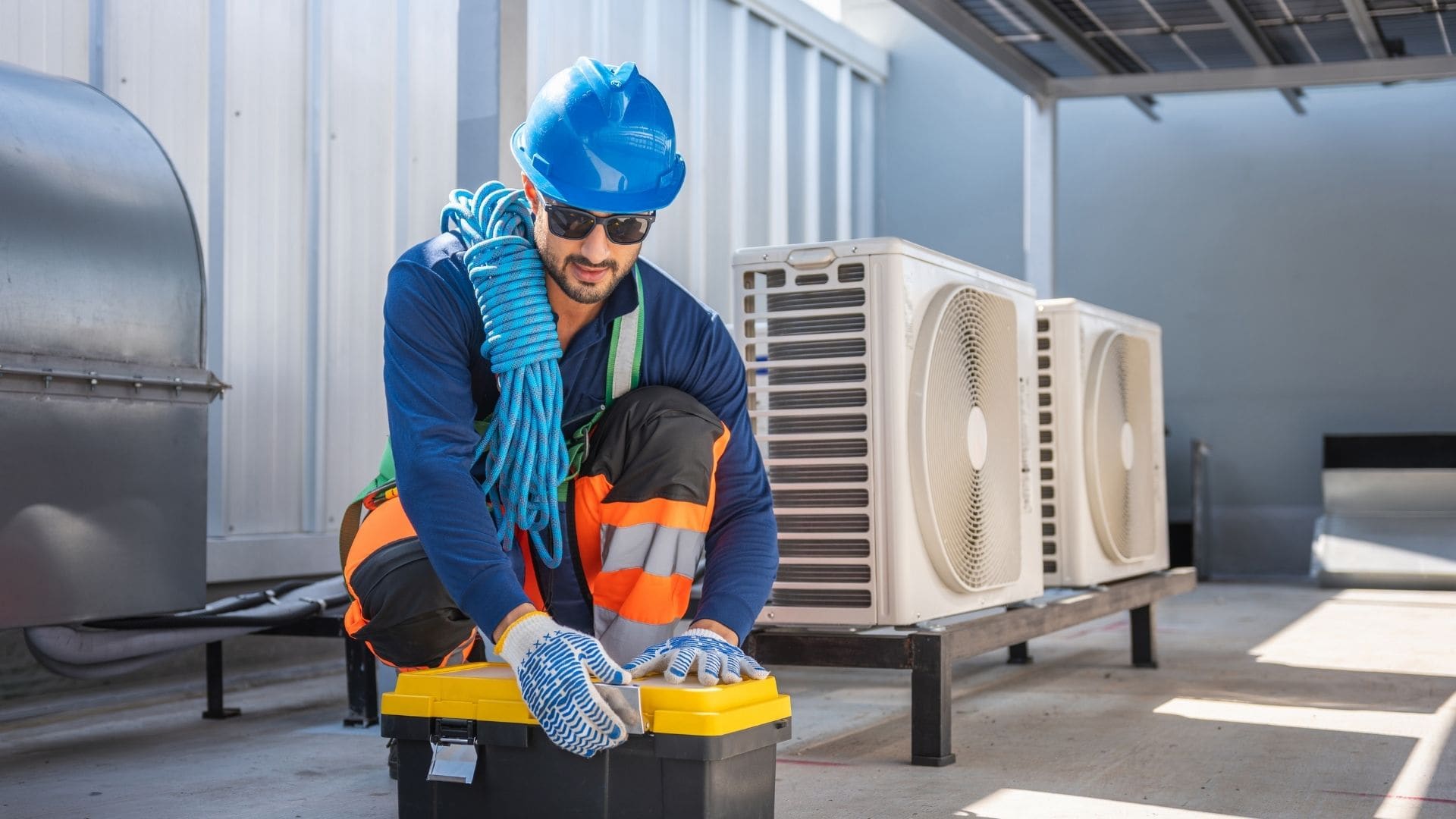 Technician in safety gear preparing equipment beside rooftop heat pump units