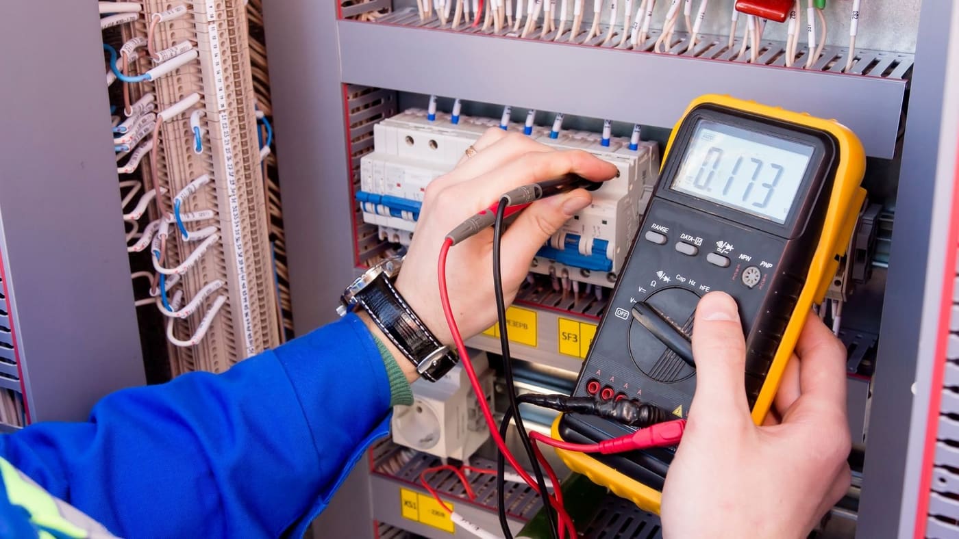 Technician measuring voltage on a commercial electrical panel with a multimeter