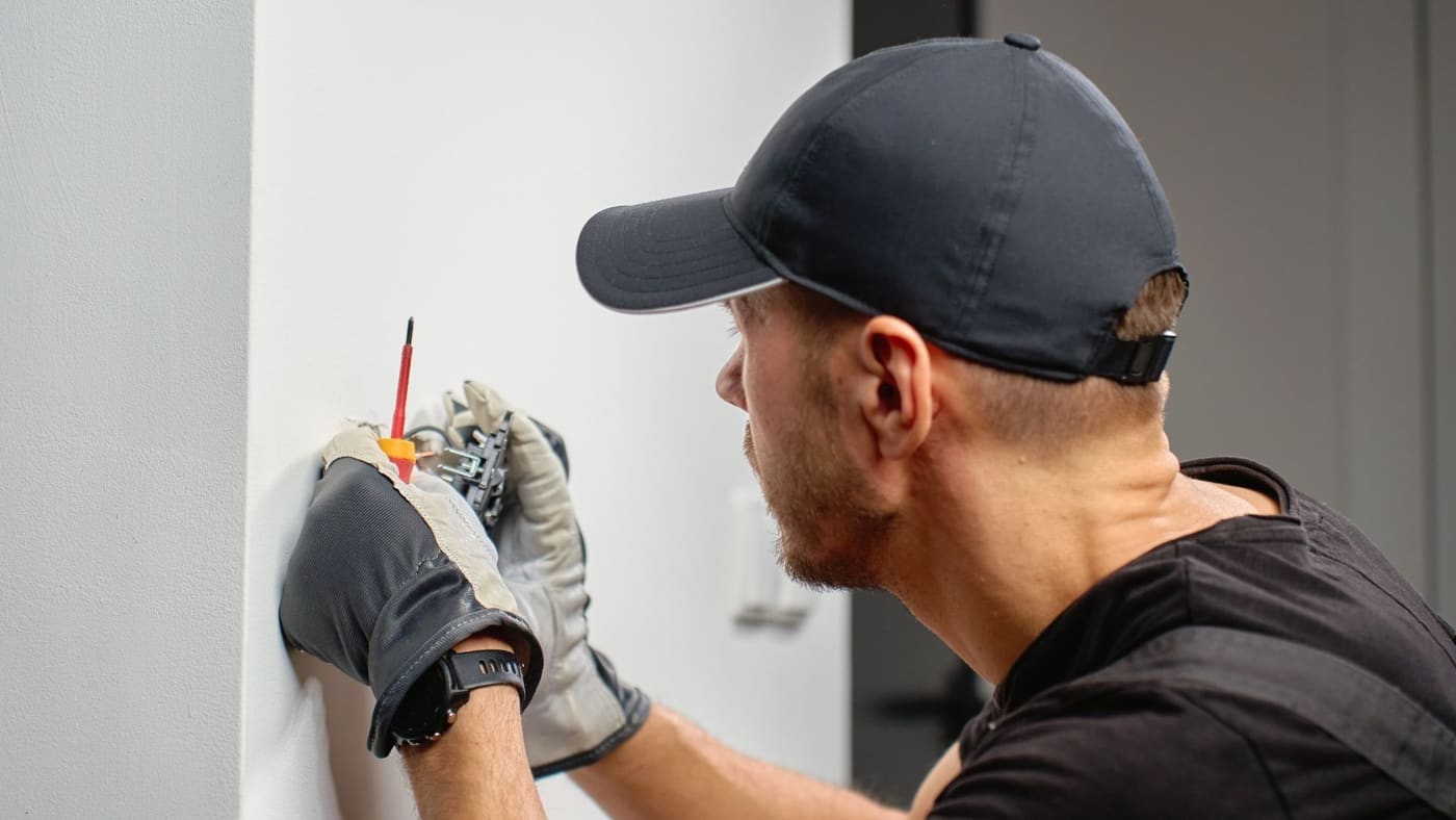 Electrician repairing a wall switch with insulated gloves and screwdriver